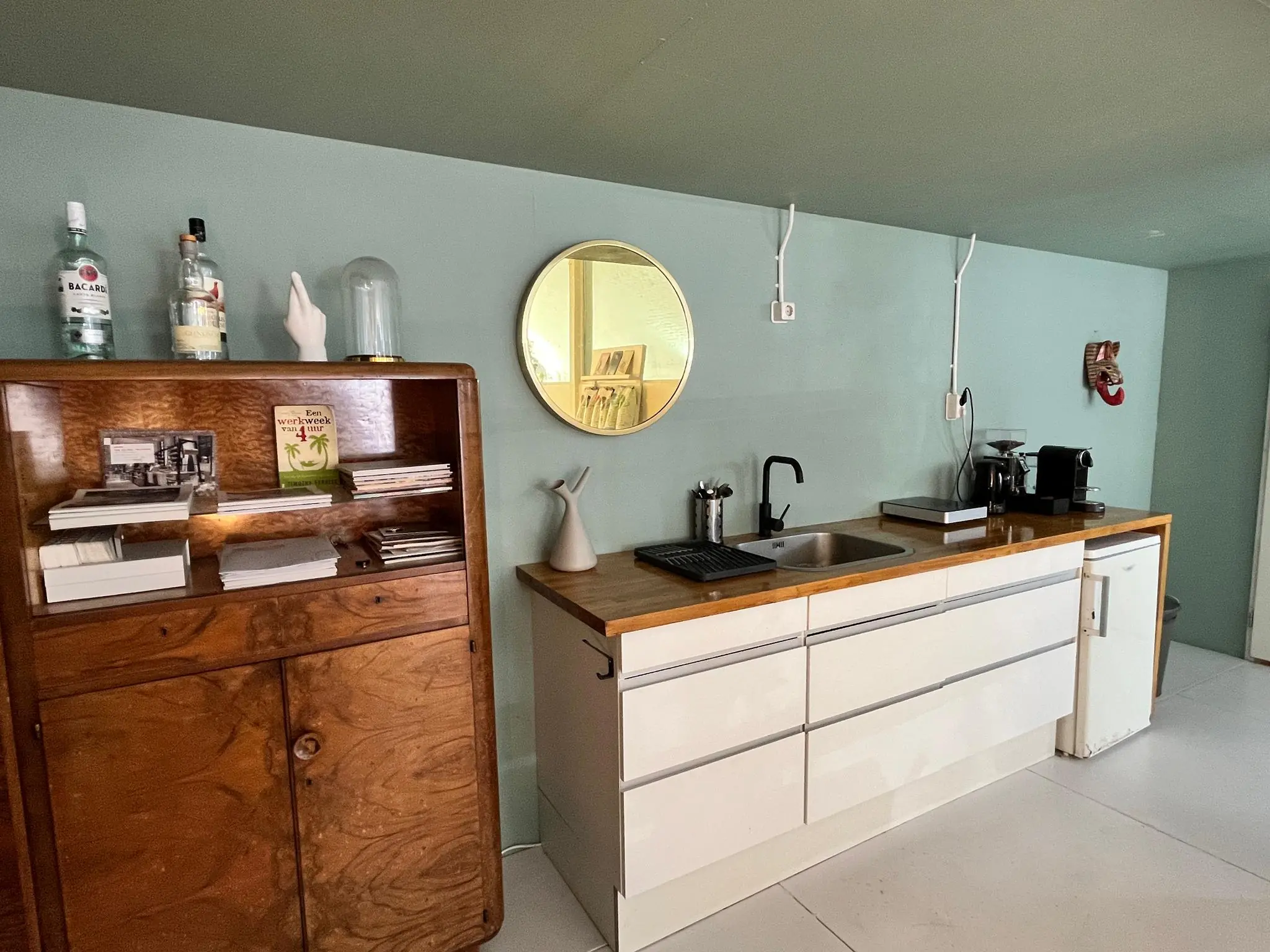 Keukenhoek met witte kasten, houten aanrechtblad, koffiemachine en wandspiegel in interieur van 'Tussen de Bogen'.